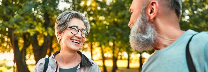 Two older adults walk and talk in a tree-lined park.